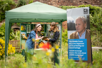 Membership recruiter speaking to woman next to a gazebo and banner in a garden