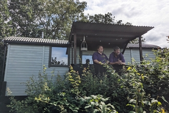 Dannie and Andrew from Leafy Fields Glamping standing on the balcony of one of the cabins at the site