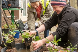 Two individuals smiling while handling potted plants.