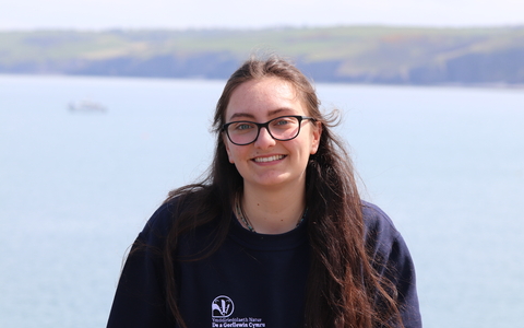 Maddy smiling at the camera, with the sea behind her