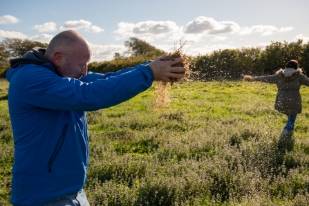 People broadcasting seeds by hand over grassy field