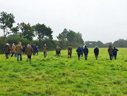 Landowners walking across grassy field alongside hedge