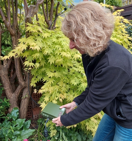 Woman holding green bat detector box in garden