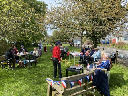 A group of people gathered in a grassy area with benches, decorated with red, white and blue bunting