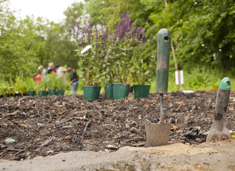 Gardening tools in the ground with flowers and a group of people in the distance