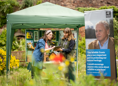 Membership recruiter speaking to woman next to a gazebo and banner in a garden